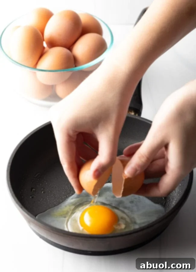 Hands cracking an egg just above a black frying pan.