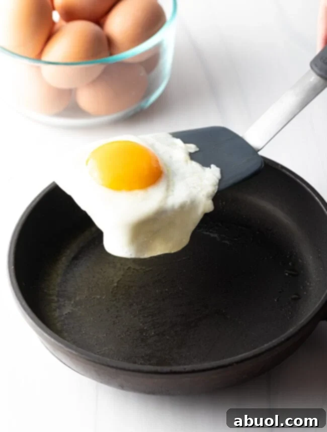 Flipping a fried egg with a black spatula over a black skillet.