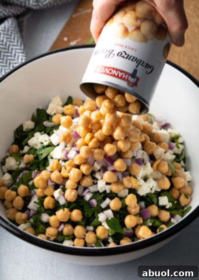 Can of chickpeas being dumped into the large white bowl with other ingredients.