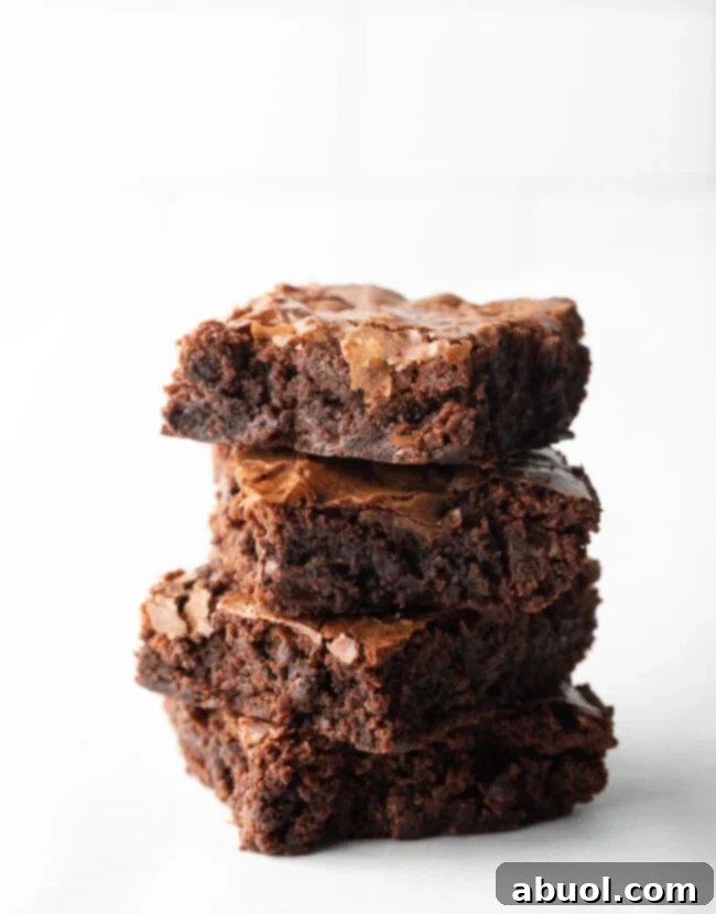 A delectable stack of four fudgy brownies, freshly baked from a homemade Ghirardelli brownie mix, presented beautifully on a pristine white background. Emphasizes rich chocolate flavor and moist texture.