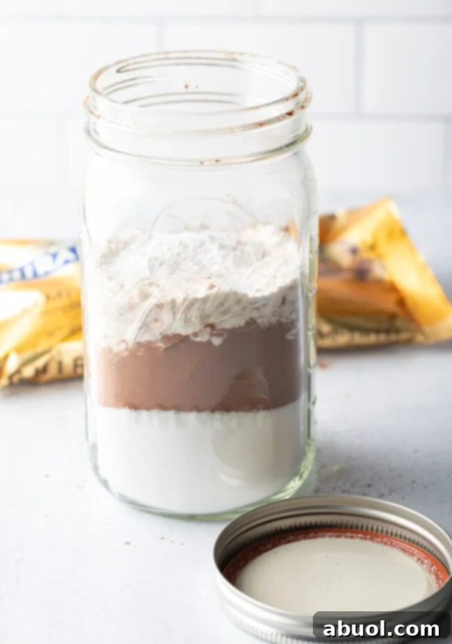 A close-up of dry ingredients being carefully layered into a mason jar, demonstrating the visual appeal and artisanal quality of a homemade brownie mix gift.