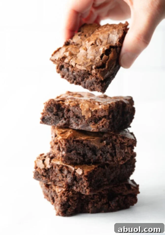 A hand gently removing a single fudgy brownie from the top of a stack of four remaining brownies, emphasizing their irresistible appeal and perfect texture.