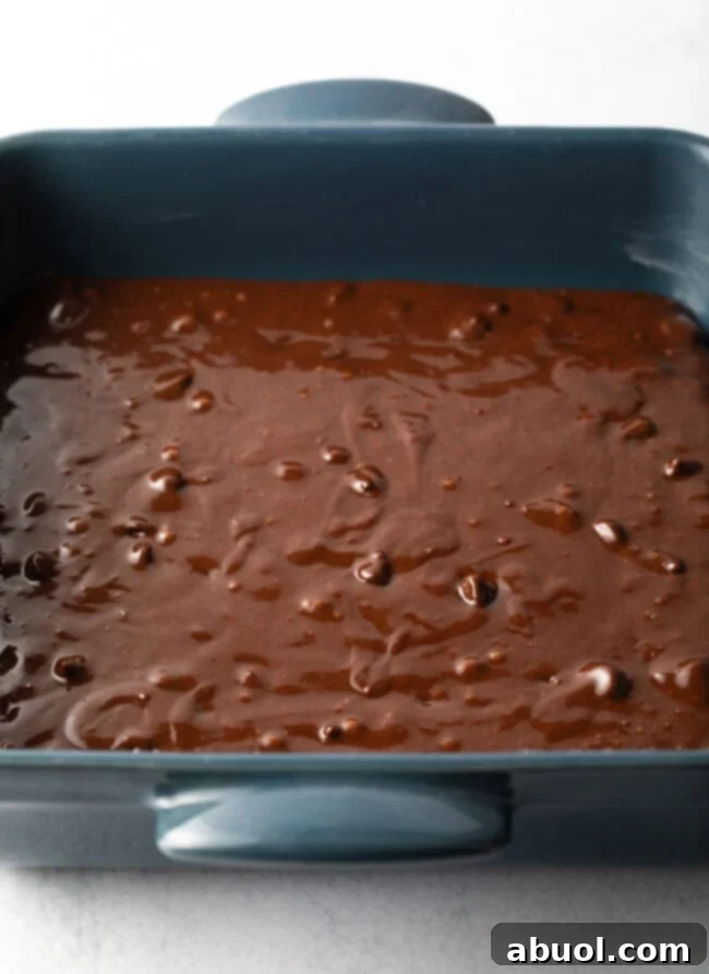 A square baking pan filled with smooth, raw chocolate brownie batter, perfectly spread and ready to be baked into fudgy goodness, highlighting preparation before baking.