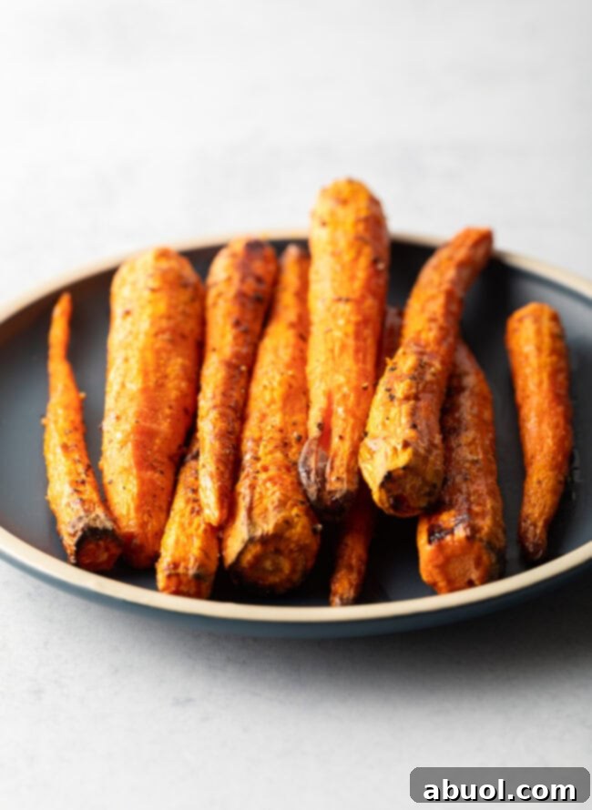 Vertical pile of air fryer roasted carrots on a round black plate.