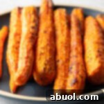 Top down view vertical pile of air fryer roasted carrots on a round black plate.