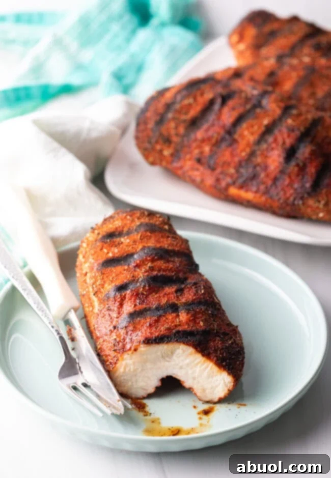 Grilled Blackened Chicken - Grilled chicken breast on a plate. The piece is cut to expose the meat inside, showing the dark, flavorful crust.