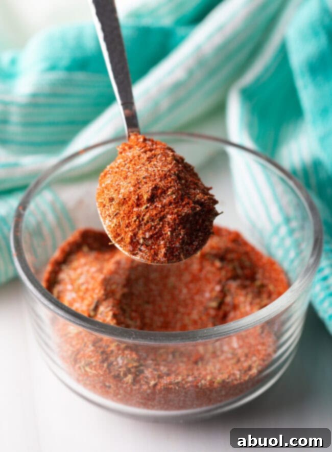 A metal spoon holds a vibrant, perfectly blended blackening seasoning, ready to be sprinkled over chicken.