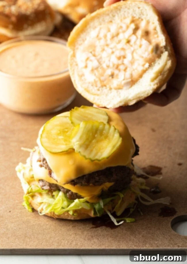Hand adding top of the burger bun to the top of the stacked ingredients.
