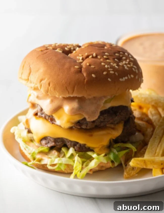 Double patty stacked cheeseburger with homemade Big Mac sauce next to a serving of french fries on a white plate.