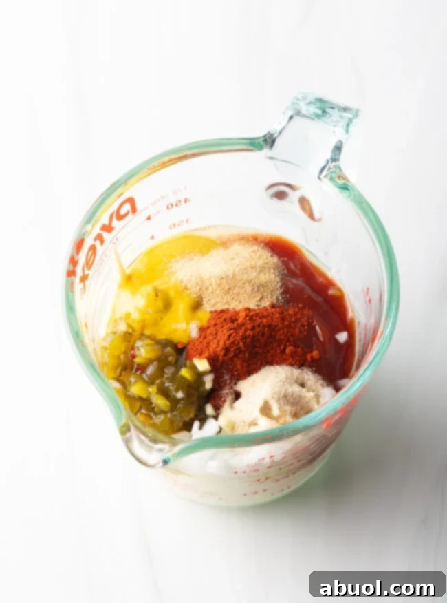 Ingredients in a glass measuring pitcher: Ketchup, mustard, mayo, pickle relish, and spices.