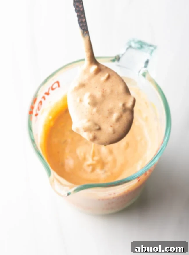 Top down view glass measuring cup with homemade burger sauce, spoonful held to camera.