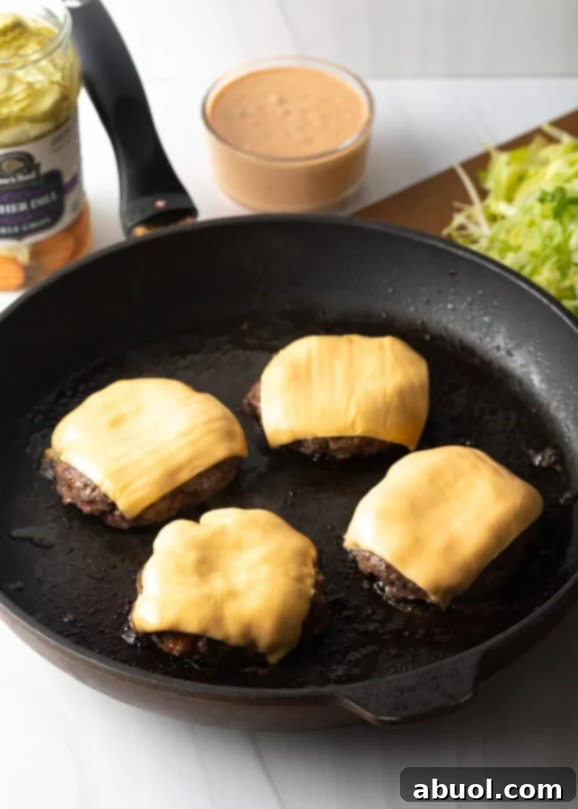 Four homecooked hamburgers with cheese in a black skillet.