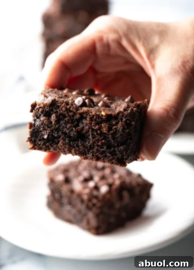 Power & Glow Collagen Brownies 4 Hand holding a fudgy brownie with a perfect bite taken out, showing its moist interior.