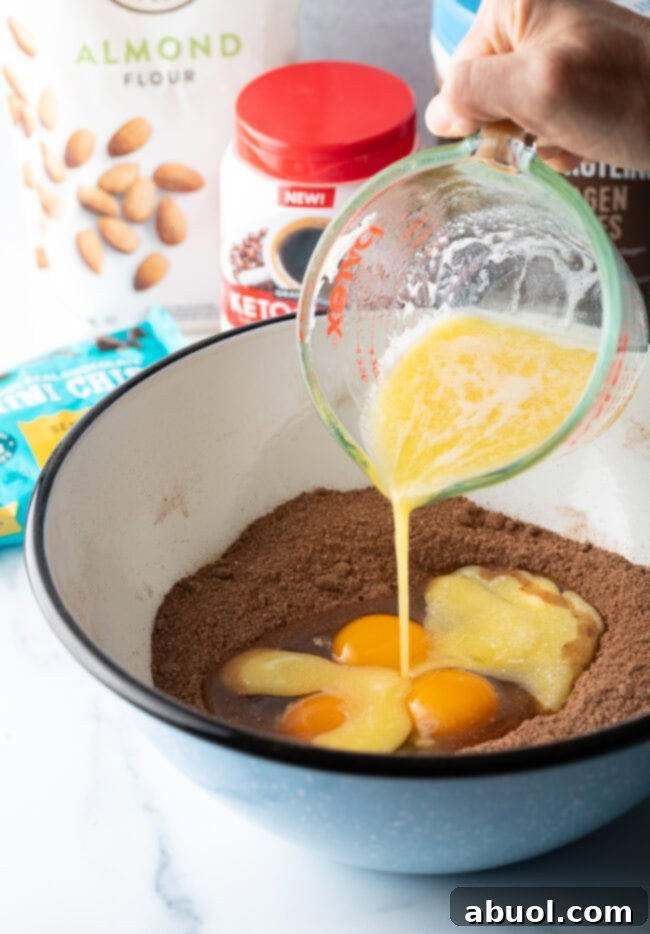 Power & Glow Collagen Brownies 7 Hand pouring melted butter and eggs from a glass measuring cup into a bowl with dry ingredients.