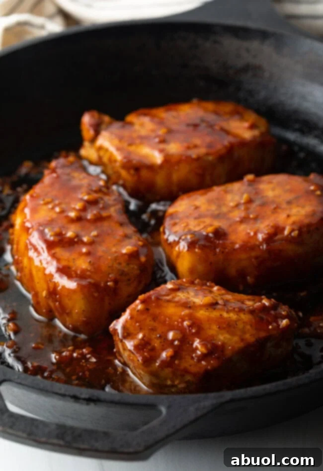Sticky Honey Garlic Pork 2 Four golden-brown pork chops nestled in a black cast iron skillet, glistening with a rich, sticky honey-garlic glaze.
