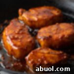 Four golden-brown pork chops nestled in a black cast iron skillet, glistening with a rich, sticky honey-garlic glaze.