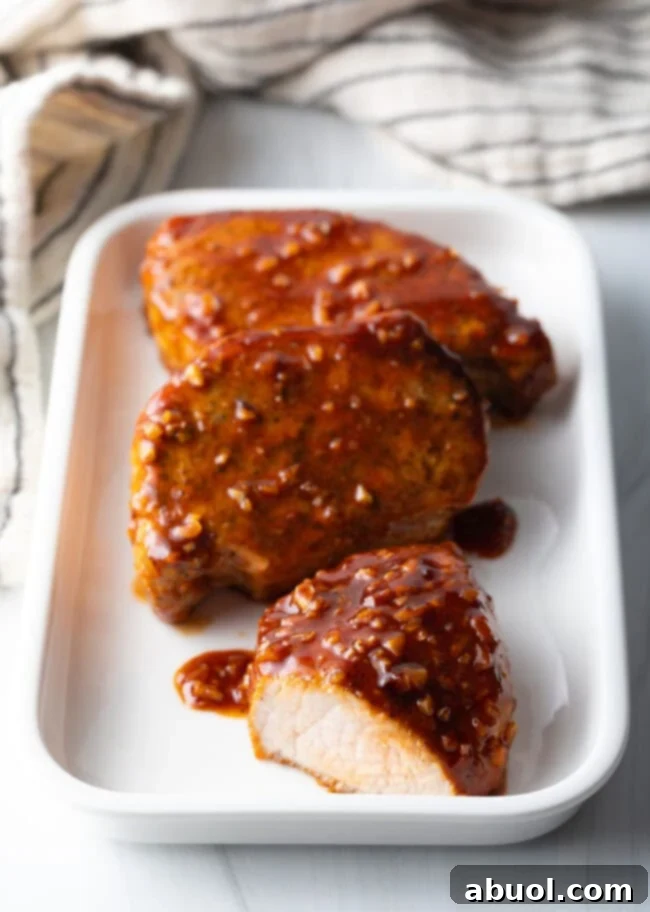 Sticky Honey Garlic Pork 3 Three perfectly glazed pork chops arranged on a rectangular white plate, showcasing the rich, sticky honey-garlic sauce. One chop is sliced to reveal its tender, juicy interior.
