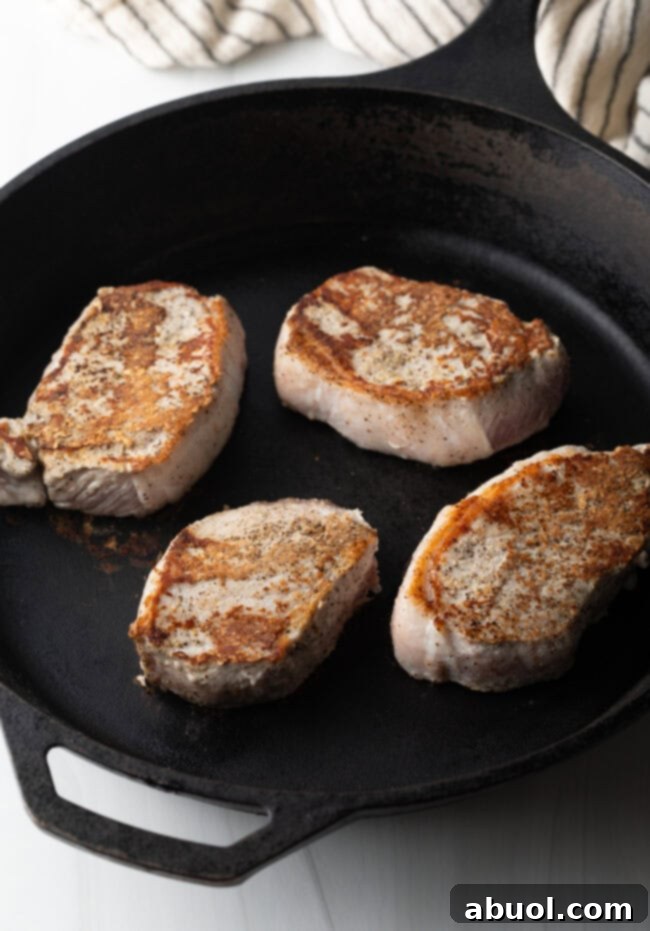 Sticky Honey Garlic Pork 6 Four pork chops, beautifully seared to a golden brown, cooking in a hot cast iron skillet.