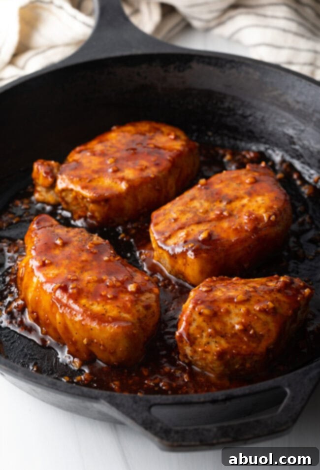 Sticky Honey Garlic Pork 7 Overhead view of four pork chops in a black cast iron skillet, now thoroughly coated in the rich, sticky honey-garlic soy sauce glaze.