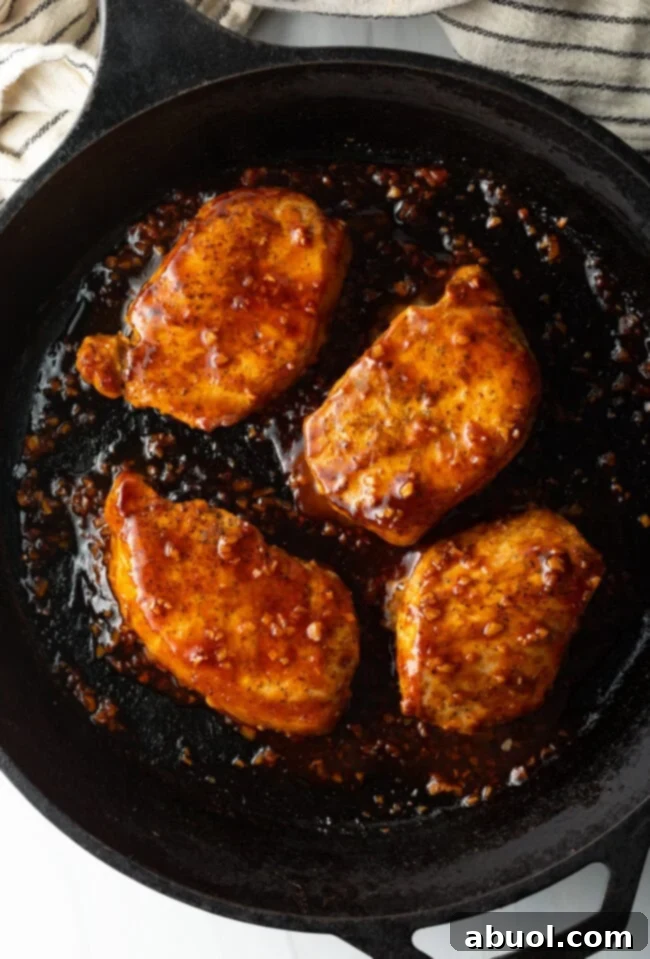Sticky Honey Garlic Pork 8 Overhead view of four pork chops in a black cast iron skillet, now thoroughly coated in the rich, sticky honey-garlic soy sauce glaze.