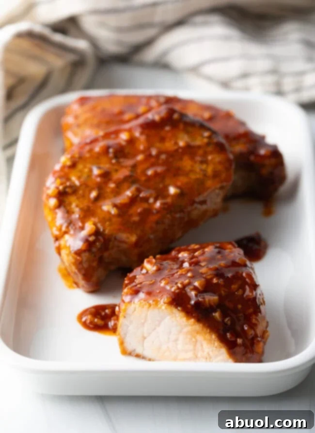 Sticky Honey Garlic Pork 10 Three perfectly glazed pork chops on a rectangular white plate, coated in the sticky honey-garlic sauce. One chop is cut open to reveal its tender, juicy interior.