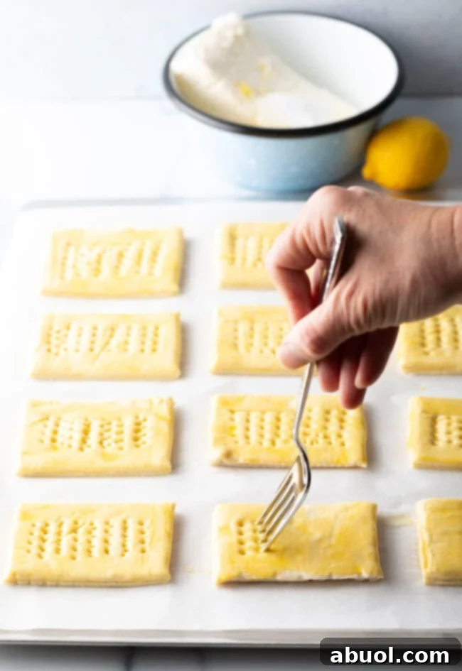Hand with fork poking holes in rectangles of puff pastry, creating a border for the filling.
