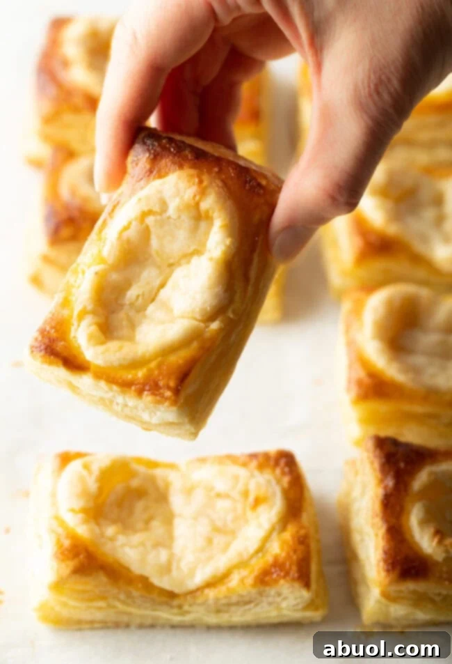 Hand holding a perfectly baked danish with cream cheese center up to the camera, inviting a bite.