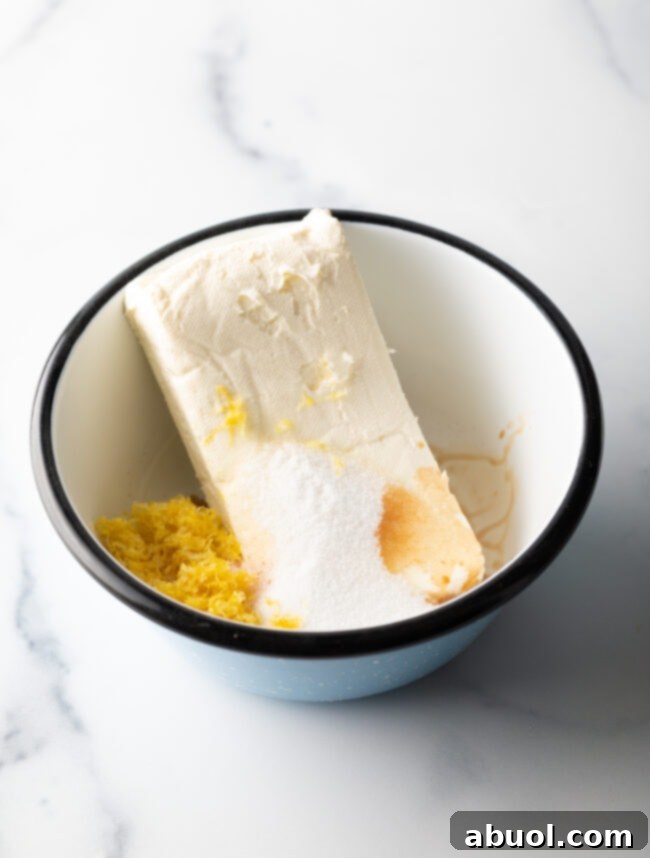 Block of cream cheese in a white bowl with fresh lemon zest, key ingredients for the filling.