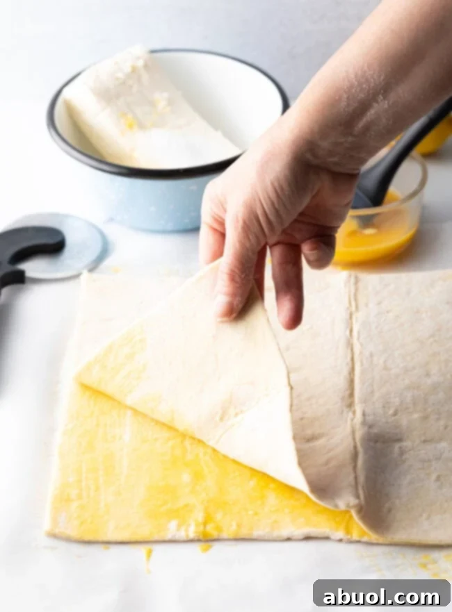 Hand adding a second layer of puff pastry on top of a brushed layer, creating multiple flaky layers.