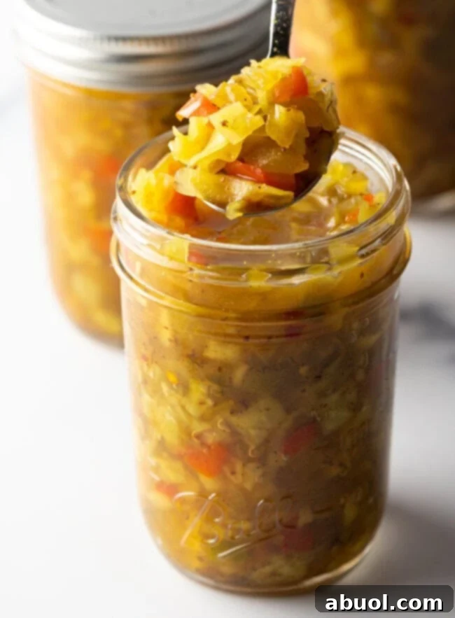 Glass jar of southern chow chow recipe. The lid is off and and a metal spoon is in the jar showing a scoop to camera.