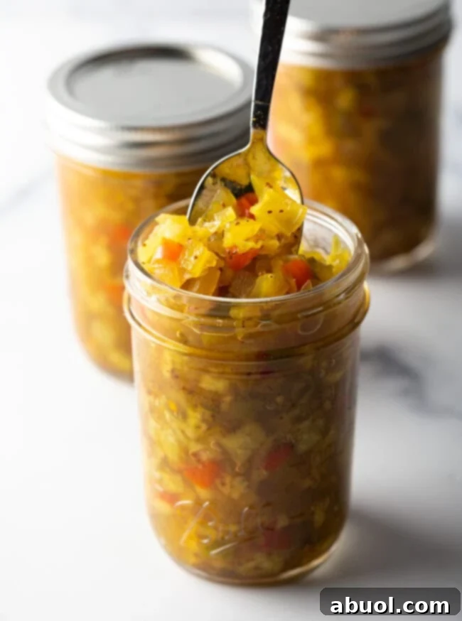 Glass jar of southern chow chow. The lid is off and to the right side, a metal spoon is in the jar showing a scoop to camera.