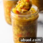 Glass jar of southern chow chow. The lid is off and a metal spoon is in the jar showing a scoop to camera.