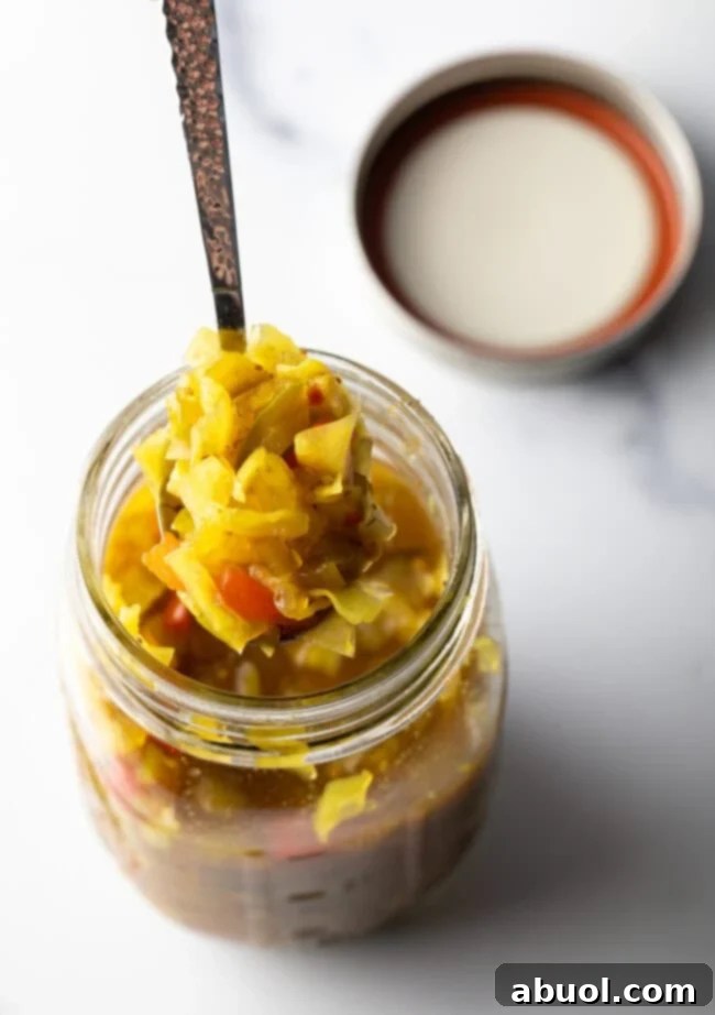 Top down view glass jar of chow chow relish. The lid is off and to the right side, a metal spoon is in the jar showing a scoop to camera.