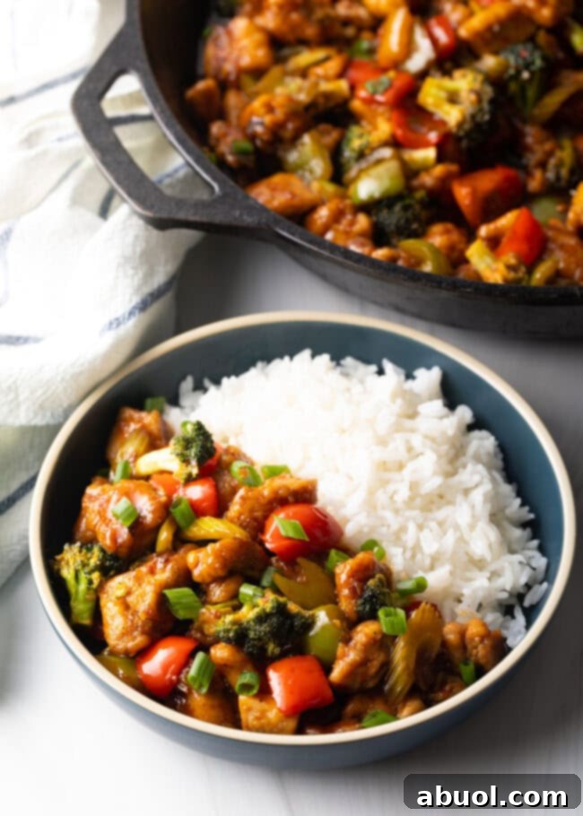 A generously filled bowl, half with savory chicken stir fry and half with white rice, showcasing a satisfying meal.