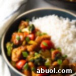 A beautifully presented bowl, half filled with savory chicken stir fry and half with fluffy white rice.
