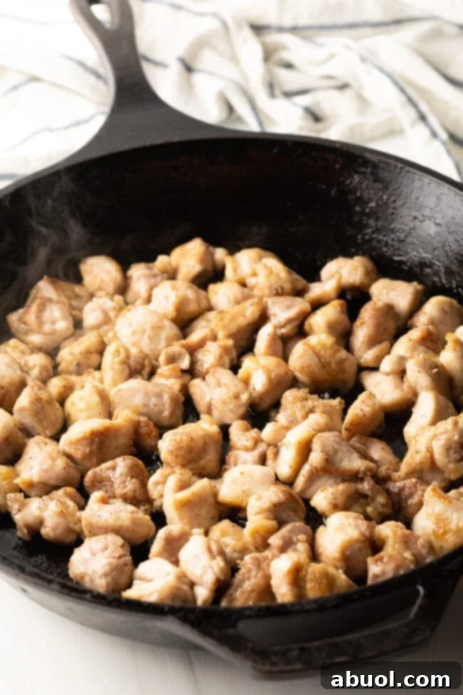 Sizzling chopped chicken thighs stir-frying in a hot cast iron skillet, acquiring a golden-brown sear.