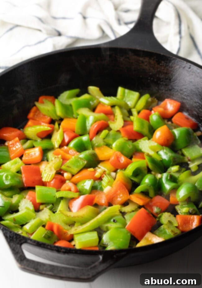 Vibrant chopped red and green bell peppers beginning to stir-fry in a cast iron skillet, retaining their fresh color.