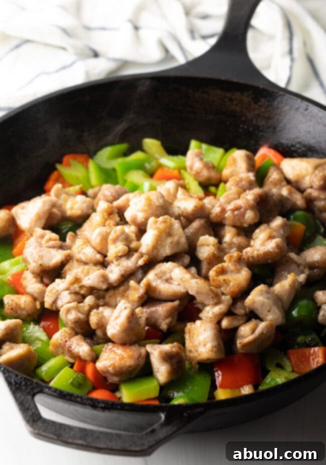 Cooked chicken pieces being added back into the skillet with sautéed vegetables, ready for the next step.