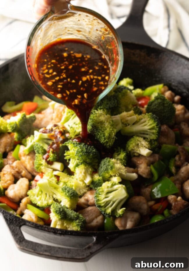 The savory Hunan sauce being poured generously over the chicken and vegetables in the hot skillet, promising rich flavor.