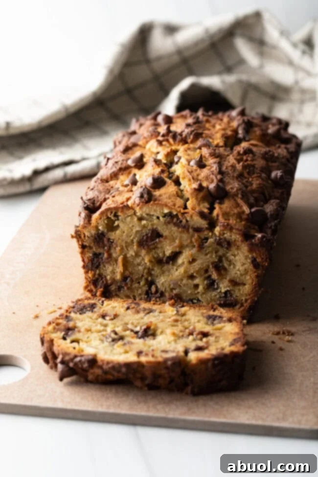 A beautifully baked loaf of high protein banana bread with chocolate chips, with one perfect slice cut and placed in front.