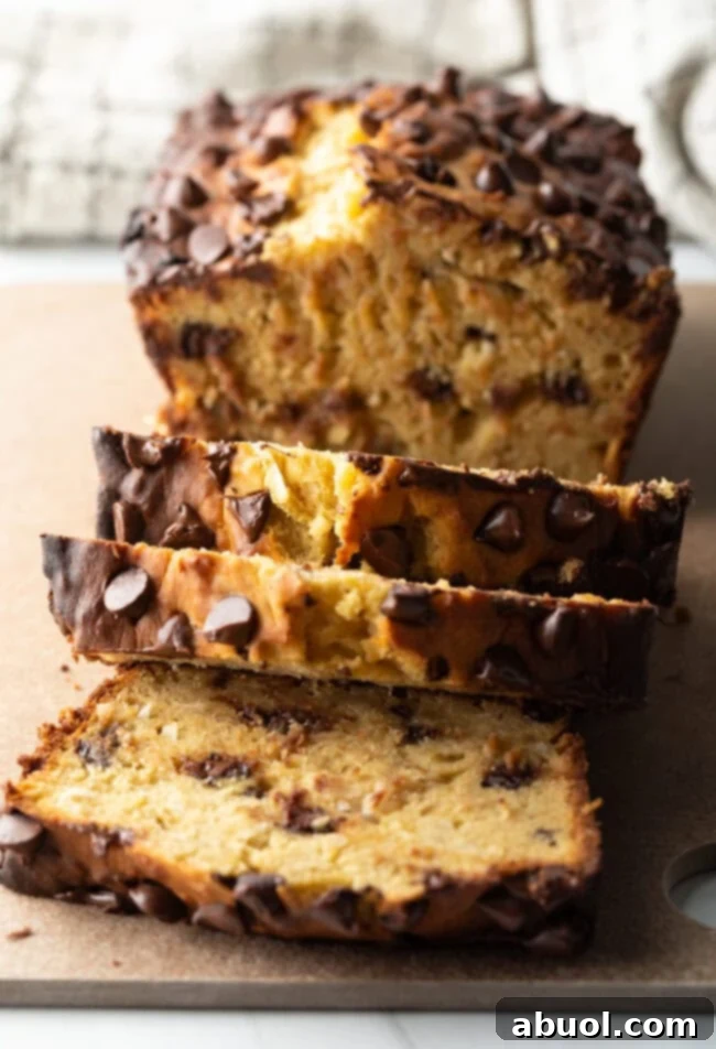 A loaf of high protein banana bread with chocolate chips, with three slices elegantly cut and displayed in front of the loaf.