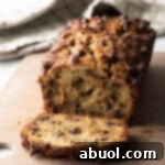 Loaf of high protein banana bread with chocolate chips. 1 slice is cut in front of the loaf.