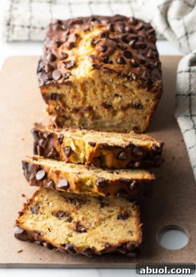 A loaf of high protein banana bread with chocolate chips, with three slices elegantly cut and displayed in front of the loaf.