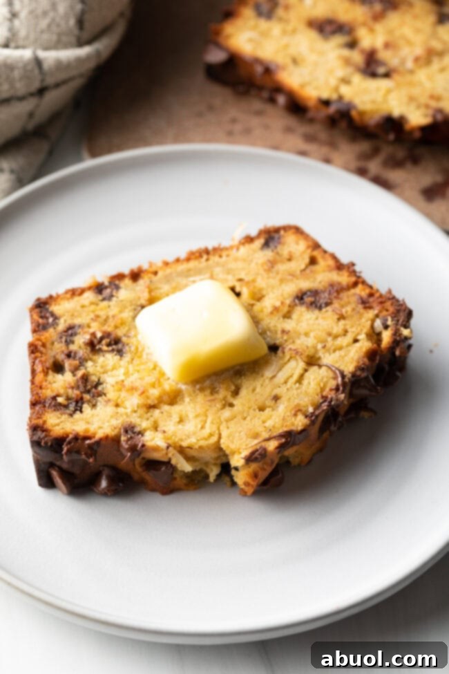 A thick slice of healthy chocolate chip banana bread on a white plate, topped with a soft pat of butter.