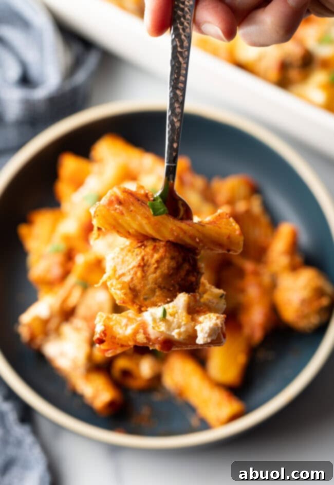Dark gray plate with a generous portion of baked meatball casserole with pasta and cheese. Fork is holding a bite to camera.