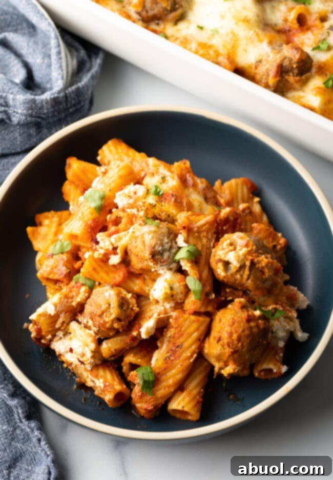 Dark gray plate with a generous portion of baked meatball casserole with pasta and cheese.