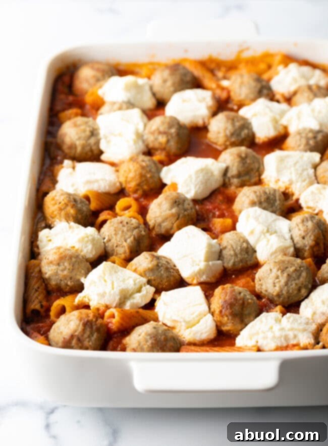 Layers of meatballs and chunks of cream cheese in marinara sauce, in white baking dish.