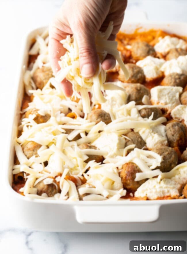 Hand adding shredded mozzarella to the casserole.