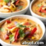 Three white and gray bowls filled with chicken taco soup, garnished with cilantro and red tortilla strips.