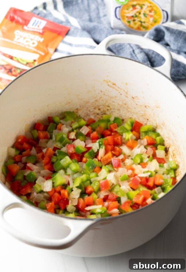 Diced bell pepper and onion being sautéed in a white cooking pot.